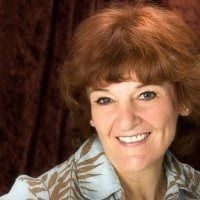 A smiling woman with short brown hair and a patterned blouse against a dark backdrop.