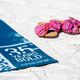 Blue towel on sand with "35 Years Bold" text; striped sandals nearby.
