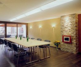 Moderner Konferenzraum mit langem Tisch, Stühlen, Steinfassade und großen Fenstern.
