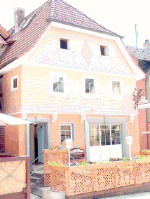 Kleines, dreistöckiges Haus mit orangefarbener Fassade und dunklem Dach in einer Stadt.