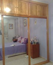 Armario con espejo en habitación de paredes lilas, cama con sábanas moradas y mesa de noche.