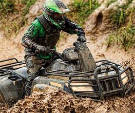 Persona conduciendo un quad cubierto de lodo en un terreno embarrado.