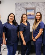 Cinco mujeres con uniformes médicos posan sonrientes en un consultorio moderno.