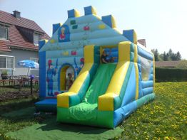 Aufblasbare Hüpfburg mit Rutsche auf einer Wiese, Kinder spielen darauf.