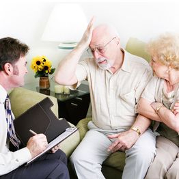 Elderly couple consulting with a professional, man appears troubled, woman offers comfort.