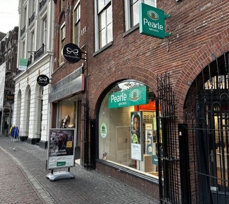Winkelstraat met Pearle opticien en andere winkels in een rij, bakstenen panden.