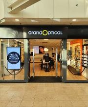Winkeluitgang van Grand Optical met reclamebord en briluitstalling aan de rechterkant.