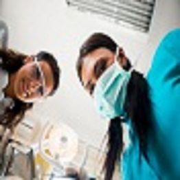 Dentists wearing masks and goggles, look down with a light above, clinic setting visible.