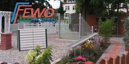 Garten mit Kieswegen, Blumenbeeten und einem Firmenschild von FEWO Kunststoffe im Hintergrund.