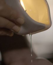 Mano vertiendo líquido de una jarra en otra palma, fondo desenfocado.