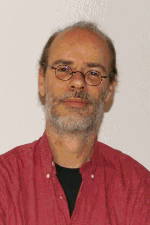 Ein Mann mit Brille und Bart in rotem Hemd vor einem neutralen Hintergrund.