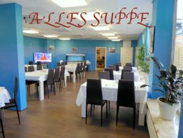 Helles Restaurant mit weißen Tischen und schwarzen Stühlen. Schriftzug "ALLES SUPPE" an der Wand.
