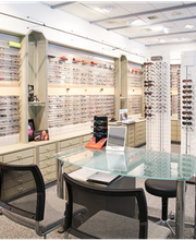 Ein Optikergeschäft mit Gläsern und Brillenfassungen auf Regalen und einem Glastisch.