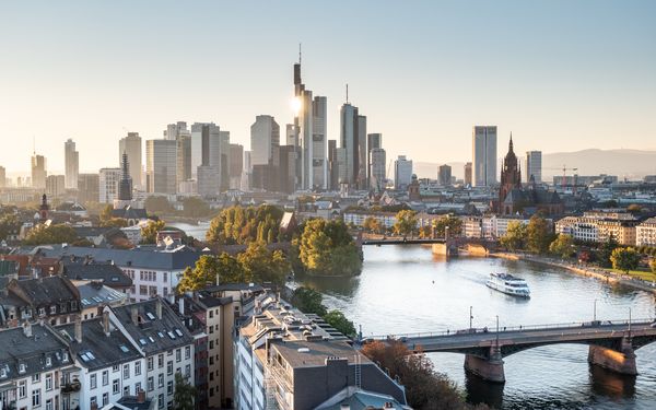 Skyline der Stadt Frankfurt im Morgengrauen, an ihr fließt der Main vorbei.