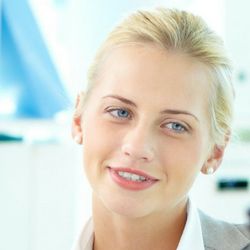 Smiling person with blonde hair and light blue eyes, wearing a white shirt.