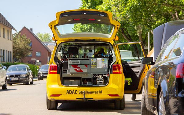 Ein Auto der ADAC Straßenwacht steht mit Warnblinker auf der Straße und hilft einem stehen gebliebenen Auto.
