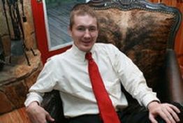 A person in a white shirt and red tie sits in a leather chair, smiling.