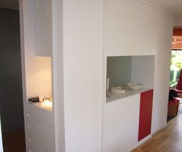 Weiße, moderne Schrankwand mit Holzfußboden, roten Akzenten und offenem Regalbereich.