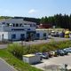 Industriegebäude mit geparkten LKWs und Autos, umgeben von Wald und einer Straße.