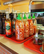 Flaschen mit Saucen und Gewürzen auf rotem Tablett auf Theke in Restaurantküche.