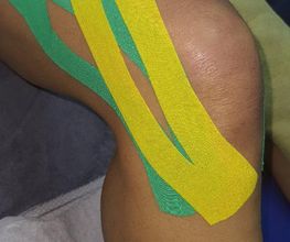 Rodilla con cintas kinesiológicas verde y amarilla aplicadas sobre la piel.