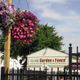 Hanging flower basket near a sign reading "Reliable Garden & Fence" with trees in the background.