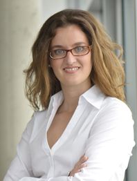 Eine Frau mit Brille und weißen Hemd lächelt in die Kamera, Arme verschränkt.