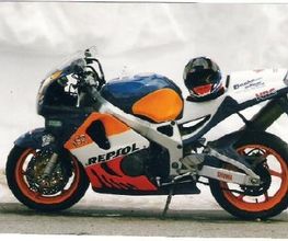 Rennmotorrad mit Repsol-Design, blau-orange-weiß. Aufsitzender Helm über dem hinteren Sitz.