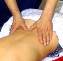 Person bei einer Rückenmassage, Hände drücken auf den unteren Rücken auf einem Massagetisch.