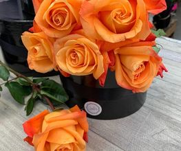 Ramo de rosas naranjas en un jarrón negro sobre una mesa de madera.