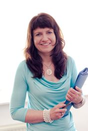 Frau in blauem Oberteil hält Ordner und lächelt.
