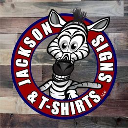 Cartoon zebra in a logo for Jackson Signs & T-Shirts on a wooden background.