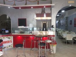 Interno di un ristorante con bancone rosso e tavoli bianchi, arredamento moderno.