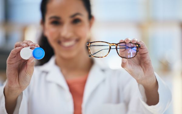 Optikerin präsentiert Kontaktlinsen in einem dafür vorgesehen Kontaktlinsenetui und Brille mit braunem Rahmen.
