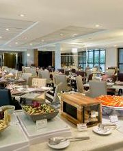 Restaurante elegante com mesas e buffet variado. Ambientes iluminados e decoração moderna.