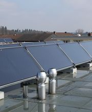 Solarmodule auf einem Flachdach in einer Wohngegend, mit Häusern und Bäumen im Hintergrund.