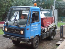Blauer Muldenkipper-LKW, beschriftet mit „Container HUPEI“, auf einem Schotterplatz.