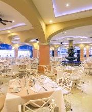 Restaurante elegante con mesas blancas, fuente central y techo iluminado.