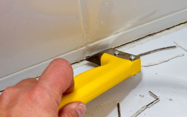 Eine alte Silikonfuge auf Fliesenspiegel wird mit Hilfe eines Fugenmessers entfernt