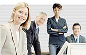 Vier Personen in Business-Kleidung, lächelnd in einem Büro.