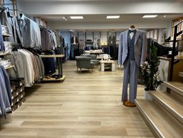 Eleganter Anzugladen mit einem ausgestellten grauen Anzug und Regalen voller Kleidung.