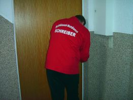 Mann in roter Jacke vom Schlüsseldienst arbeitet an einer Tür in einem Treppenhaus.