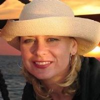 A person wearing a straw hat smiles at sunset by the sea.