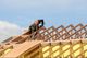 Worker installing wooden roof trusses on a building under clear blue sky.