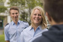 Zwei Polizist*innen sprechen im Freien mit einer Person. Alle tragen blaue Uniformen.