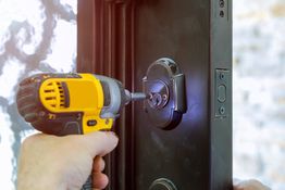 Hand boort slot in zwarte deur met elektrische schroevendraaier.