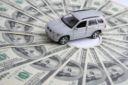 A toy car sits on a fan of 100-dollar bills, symbolizing car expenses or investment.