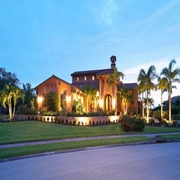 Modern villa with palm trees and warm lighting against a blue sky backdrop at dusk.