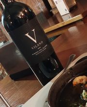 Botella de vino tinto y copa junto a un plato de camarones en una mesa de madera.