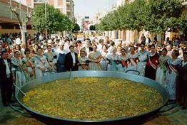 Gruppe von Menschen in traditionellen Kostümen um eine riesige Paella im Freien versammelt.